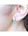 Close-up of an ear wearing an emerald stud earring with a blurred background