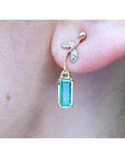Close-up of dangle colombian emerald earring in 14k yellow gold on a person's ear.