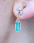 Close-up of dangle emerald earrings yellow gold on a person's ear.