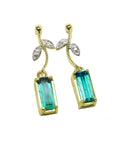Front position of a pair of emerald dangle earrings in 14k yellow gold, pending from a leafy stem