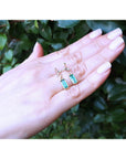 Hand displaying two emerald gemstone earrings with a green leafy background