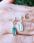Top and underside gold emerald earrings held on a hand against a blurred natural background
