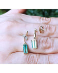 Top and underside gold emerald earrings held on a hand against a blurred natural background