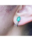 Pear-shaped emerald clip-on earring with accent diamonds in 14K white gold, worn on an ear.