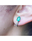 Pear-shaped emerald clip-on earring with accent diamonds in 14K white gold, worn on an ear.