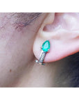 Pear-shaped emerald clip-on earring with accent diamonds in 14K white gold, worn on an ear.