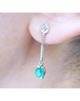 Close-up of a natural emerald teardrop earring with a diamond on a person's ear.