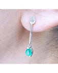 Close-up of a natural emerald teardrop earring with a diamond on a person's ear.