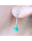 Close-up of an emerald green teardrop earring with a diamond on a person's ear.