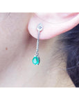 Close-up of a May's birthstone emerald dangle earring worn by a person.