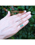 Hand exposing a 14k gold emerald dangle earrings against a green leafy background