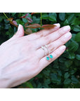 Pear-shaped Muzo Colombian emerald dangle earrings in 14K white gold with diamonds, worn on a hand.