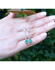 Pear-shaped Muzo Colombian emerald dangle earrings with diamonds in 14K white gold on a hand.