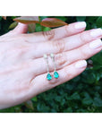 Pear-shaped Muzo Colombian emerald dangle earrings with diamonds in 14K white gold on a hand.