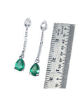 Pear-shaped Muzo Colombian emerald dangle earrings in 14K white gold with diamonds, next to a ruler.