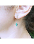 Close-up of woman's ear wearing a teardrop emerald earring with a blurred background