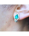 Pear-shaped Colombian emerald and diamond 14K gold clip/post earring on an ear.
