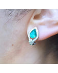 Pear-shaped Colombian emerald and diamond 14K gold clip/post earring on an ear.