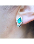 Pear-shaped Colombian emerald and diamond 14K gold clip/post earring on an ear.
