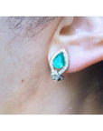 Pear-shaped Colombian emerald and diamond 14K gold clip/post earring on an ear.