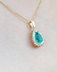 Teardrop-shaped pendant with a natural emerald on a gold chain against a light pink skin background
