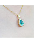 Teardrop-shaped pendant with a natural emerald on a gold chain against a light pink skin background
