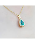 Teardrop emerald pendant with a diamond halo on a gold chain, worn on a woman's neck.
