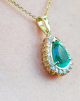 Gold pendant with a teardrop emerald on a light pink skin background