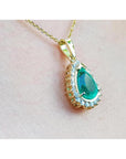 Teardrop emerald pendant with diamond halo on a gold chain, worn on a person.