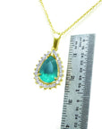 Gold necklace with a natural emerald teardrop pendant next to a ruler for scale on a white background