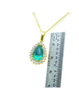 Gold necklace with a natural emerald teardrop pendant next to a ruler for scale on a white background