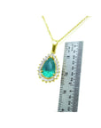 Teardrop Colombian emerald pendant with diamond halo on a gold chain, next to a ruler.