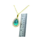 Teardrop Colombian emerald pendant with diamond halo on a gold chain, next to a ruler.
