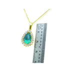 Teardrop Colombian emerald pendant with diamond halo on a gold chain, next to a ruler.