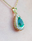 Gold pendant with a natural teardrop-shaped emerald on a light pink skin background