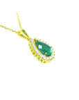 A yellow gold necklace with a natural teardrop emerald pendant on a white background