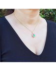 Teardrop emerald pendant with diamond halo on a gold chain, worn by a woman.