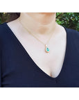 Teardrop emerald pendant with diamond halo on a gold chain, worn by a woman.