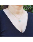 Teardrop emerald pendant with diamond halo on a gold chain, worn by a woman.