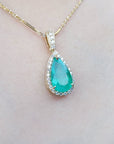 Teardrop-shaped genuine colombian emerald pendant on a gold chain against a skin background