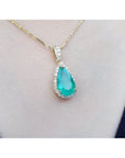 Teardrop-shaped genuine colombian emerald pendant on a gold chain against a skin background