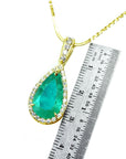 A natural colombian emerald teardrop pendant on a gold chain with a ruler for scale on a white background