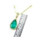 A natural colombian emerald teardrop pendant on a gold chain with a ruler for scale on a white background