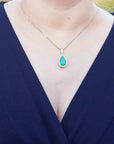 A natural Muzo mine colombian emerald teardrop pendant necklace on a woman wearing a navy-blue top.