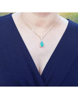 A natural Muzo mine colombian emerald teardrop pendant necklace on a woman wearing a navy-blue top.