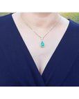 18K yellow gold teardrop emerald pendant with halo diamonds on a woman's neck.