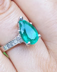 Teardrop emerald ring with diamonds on a finger.