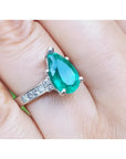 3.09 ct pear-shaped deep bluish-green emerald ring with princess cut diamonds in 14K white gold.