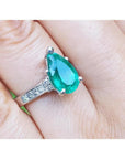 3.09 ct pear-shaped deep bluish-green emerald ring with princess cut diamonds in 14K white gold.