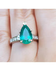 A Colombian emerald teardrop ring and princess cut band diamonds on a hand.